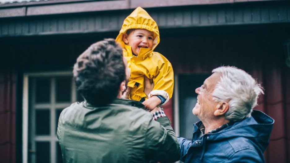Photo of smiling little boy playing with his father and grandfather in the backyard