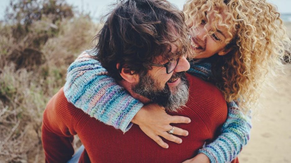 One man carrying overjoyed woman in piggyback in outdoor leisure activity together having fun and laughing a lot. Happy mature people youth inside enjoy relationship and friendship.