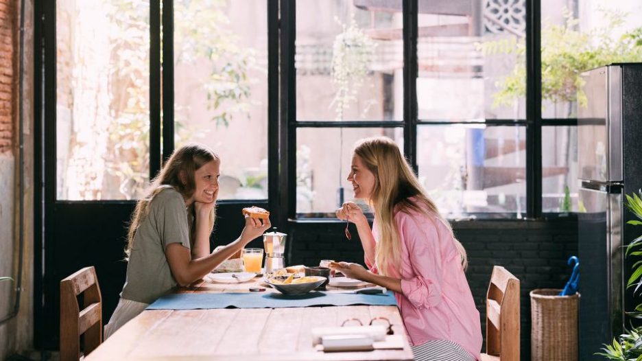 Two young women gossiping at a cafe over breakfast