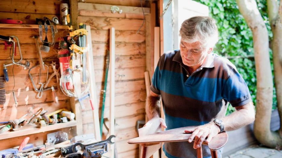 mature man is working with a wooden chair in his shed with tools and natural light
