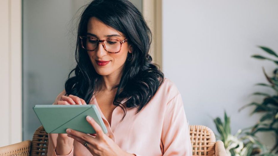 thoughtful and smiling woman wearing glasses while she uses her tablet