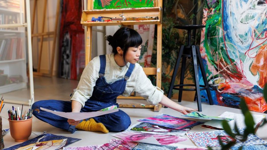 female artist arranging various paintings on floor