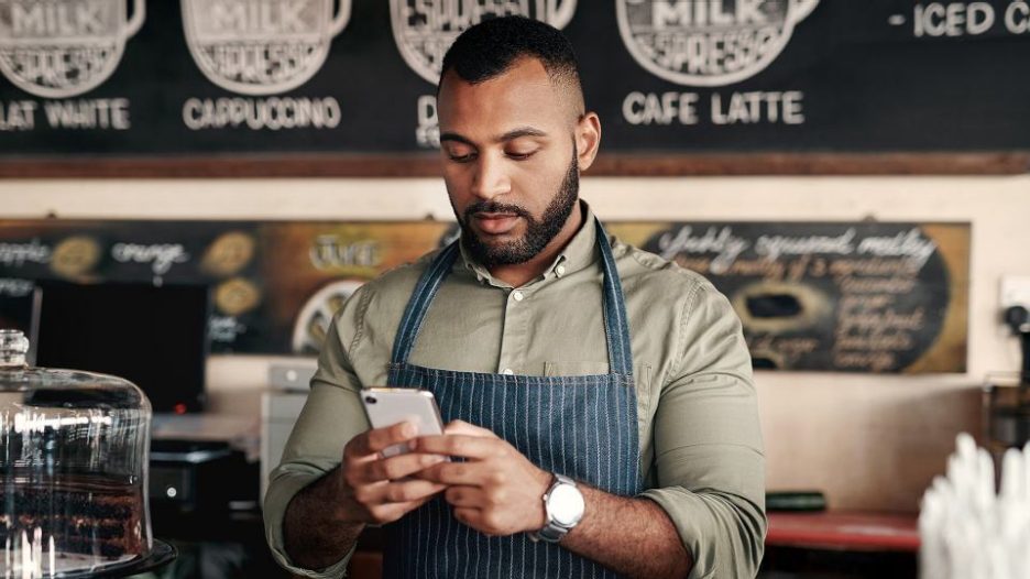 cafe owner in a striped apron is checking his phone in a quiet moment