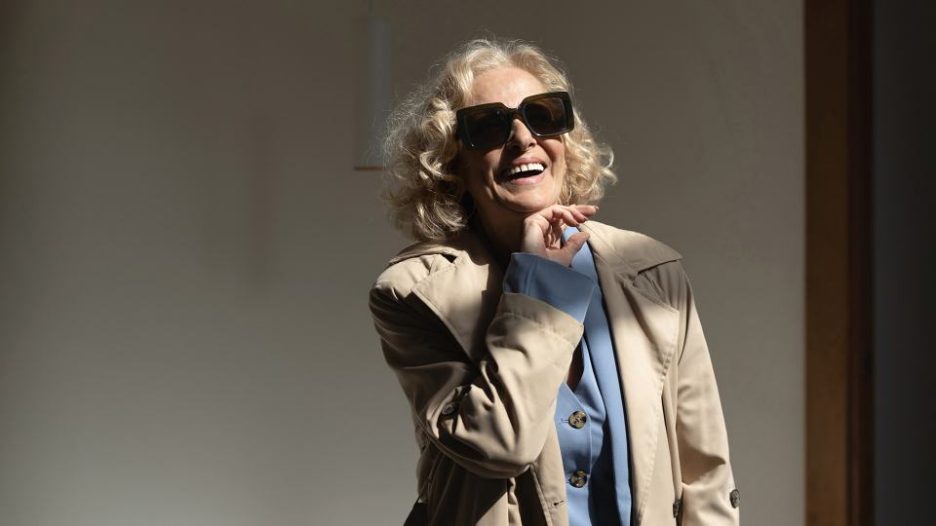 senior woman in stylish sunglasses and a trench coat over a blue suit