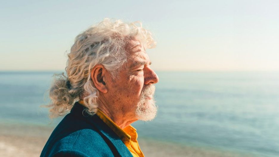 senior man looking into the sun at the beach