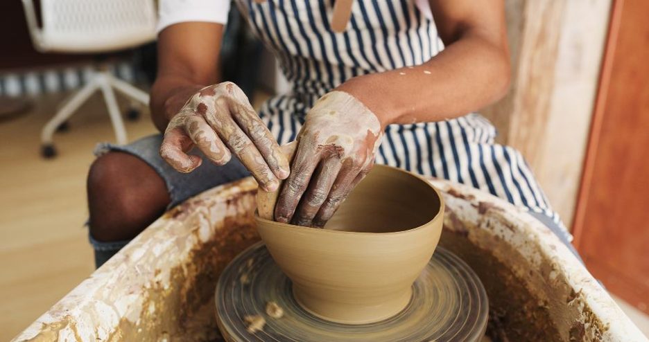 close up of a woman in a striped apron creating a clay bowl on a wheel