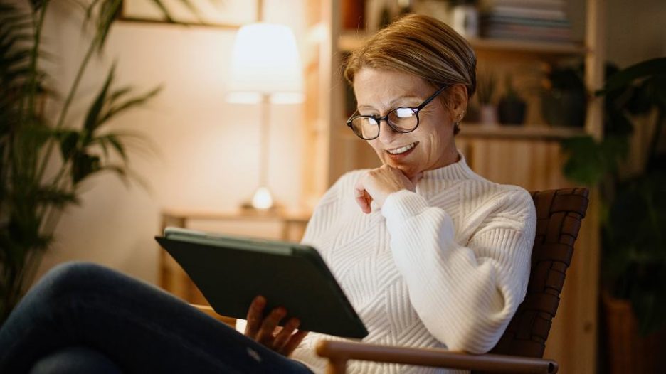 woman in a cream jumper relaxing in a comfortable chair at home while reading her tablet