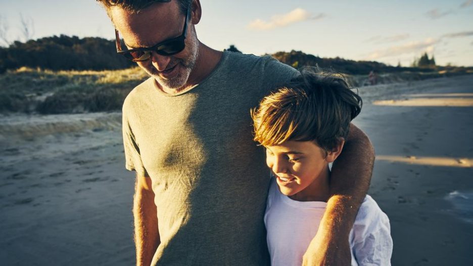 father and sun hug while walking on a beach in the late afternoon