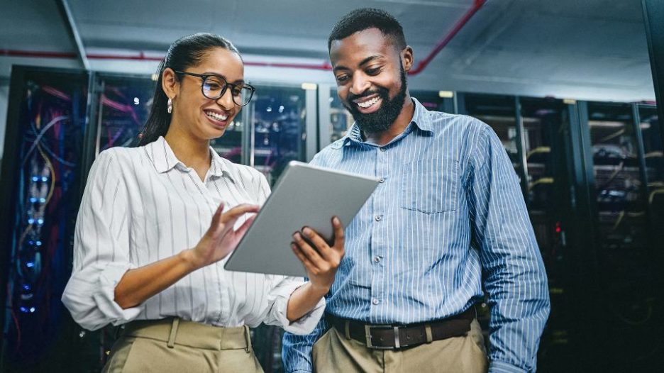 happy male and female it professionals are looking at a tablet while standing in the server room