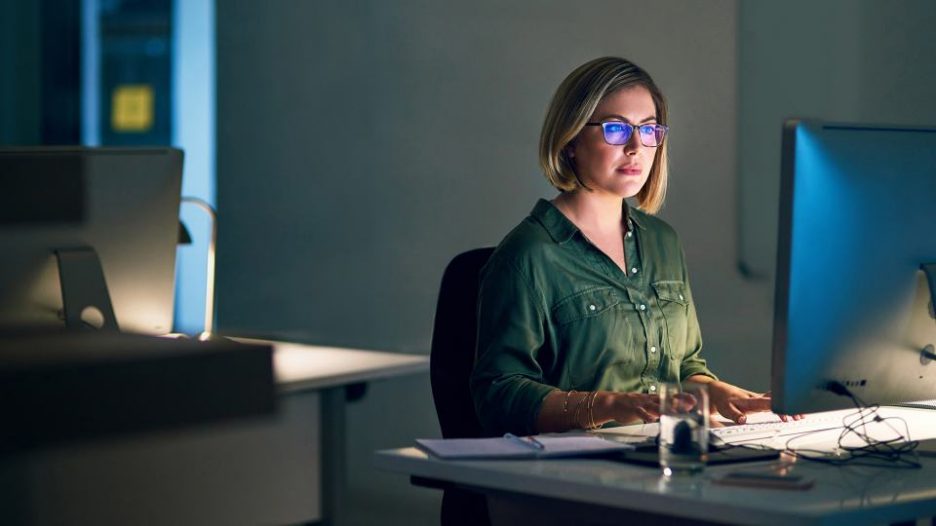 a woman in glasses calmly working at her computer late at night