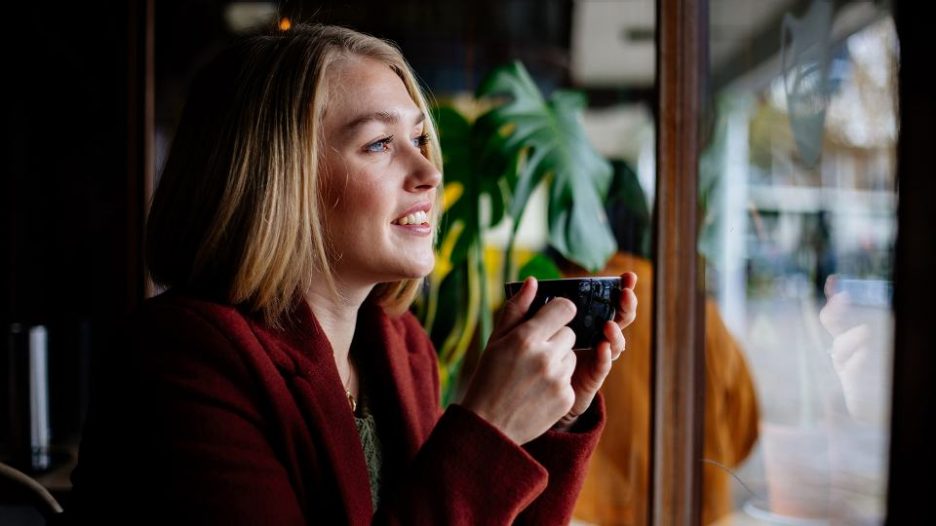 Female holding coffee mug smiling and looking downwards out of window