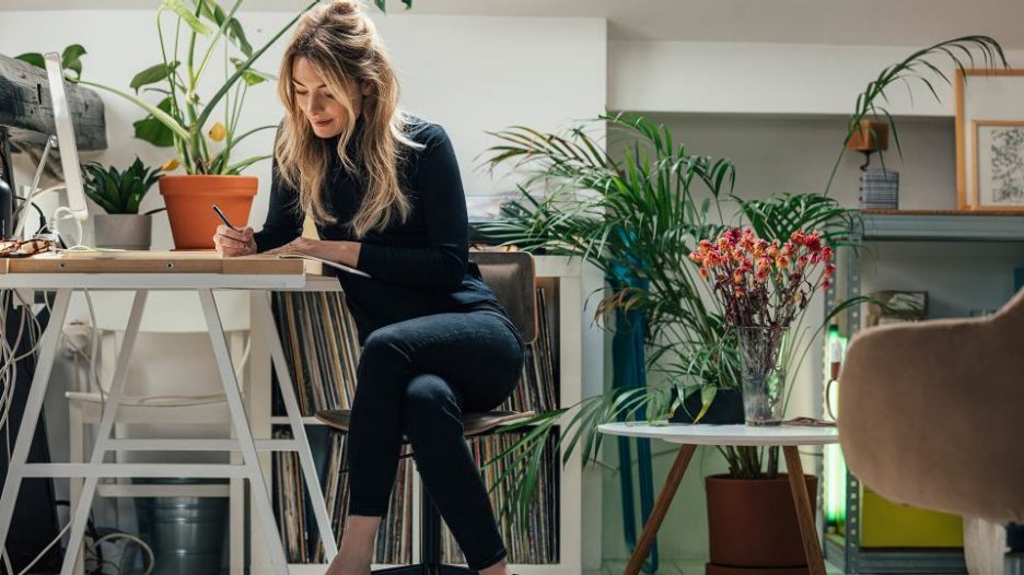 woman writing in a notebook while sitting at a table in her bohemian styled home