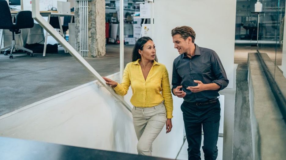 Shot of two colleagues discussing while walking up the stairs in a modern office. Two business people in a motion on stairs in the office.