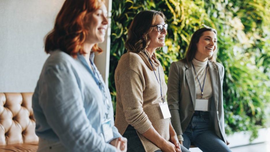 Diverse business professionals engage in a lively meeting in an office. Their teamwork and communication skills shine through as they discuss ideas and collaborate. Smiling and happy, they showcase a positive work environment. This conference-like event highlights networking and panel discussions.