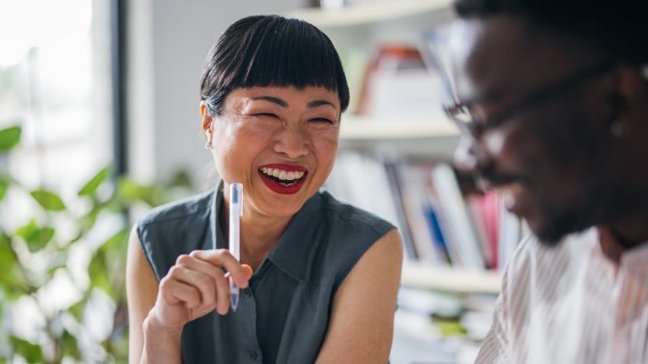 Japanese entrepreneur laughing while holding a pen and talking to her coworker.