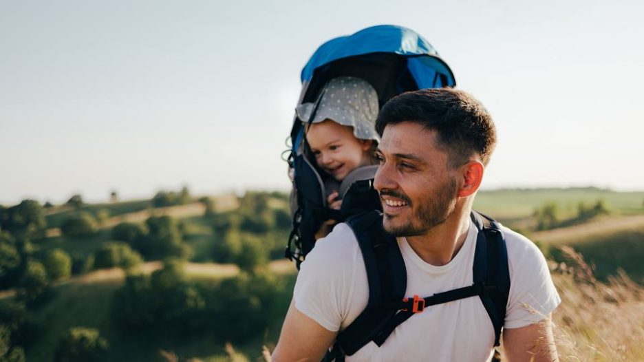 happy father is carrying his baby in a backpack during a walk in the countryside