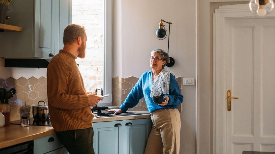 senior woman and young man standing in kitchen talking
