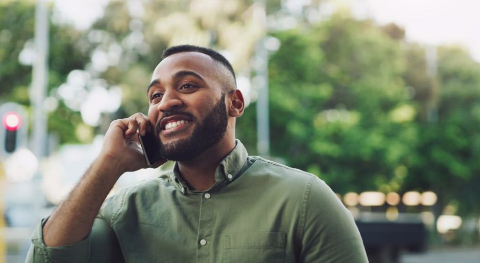 happy man in a green shirt is on the phone while outside