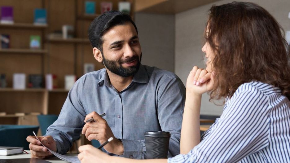 professional male and female having a relaxed office meeting while drinking coffee and taking notes