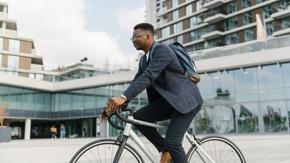 Young businessman riding a bicycle to work in the urban city zone with buildings in the background