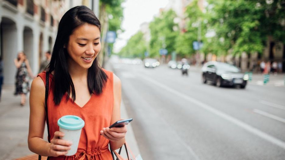 woman on a street with coffee looking at her phone