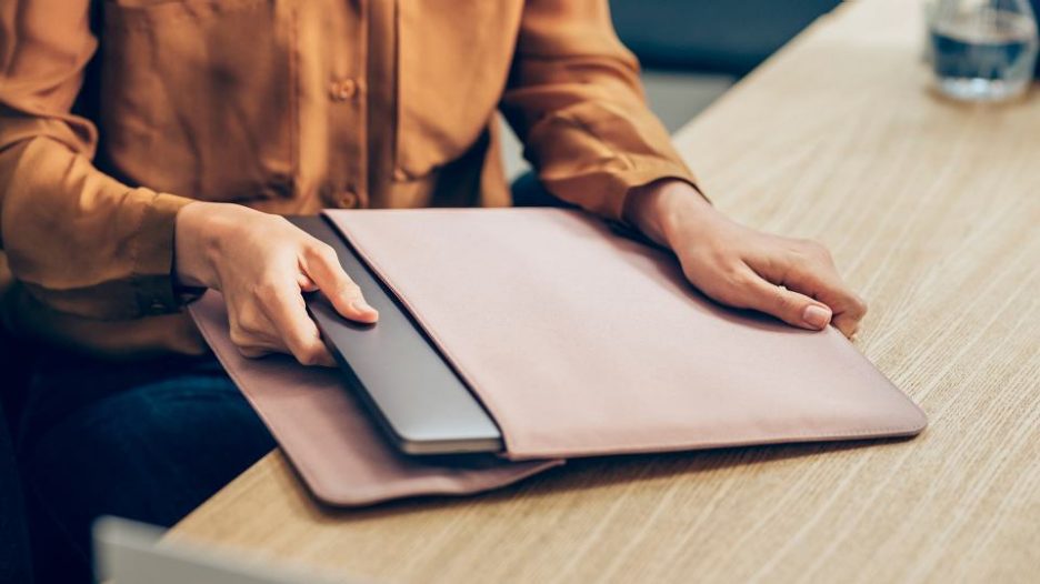 close up of a person in a burnt orange shirt removing their laptop from its case on a desk