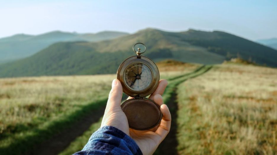 person holding compass in hand on mountains road