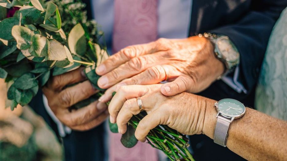 elderly couple holding flowers together while hands