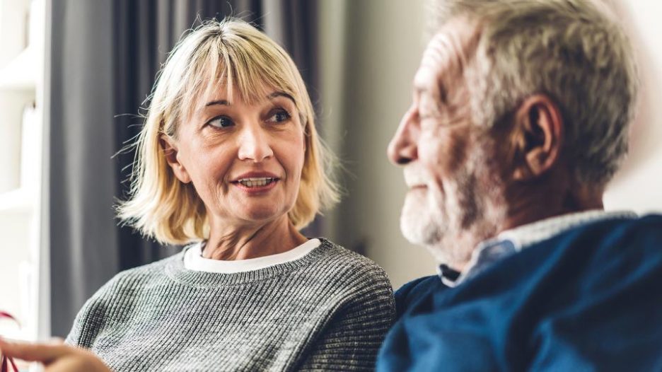mature woman is talking to a senior man as they sit inside their home