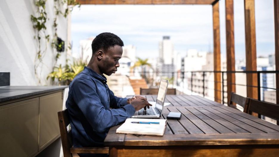 serious man is working at a laptop while sitting at an outside table on a patio